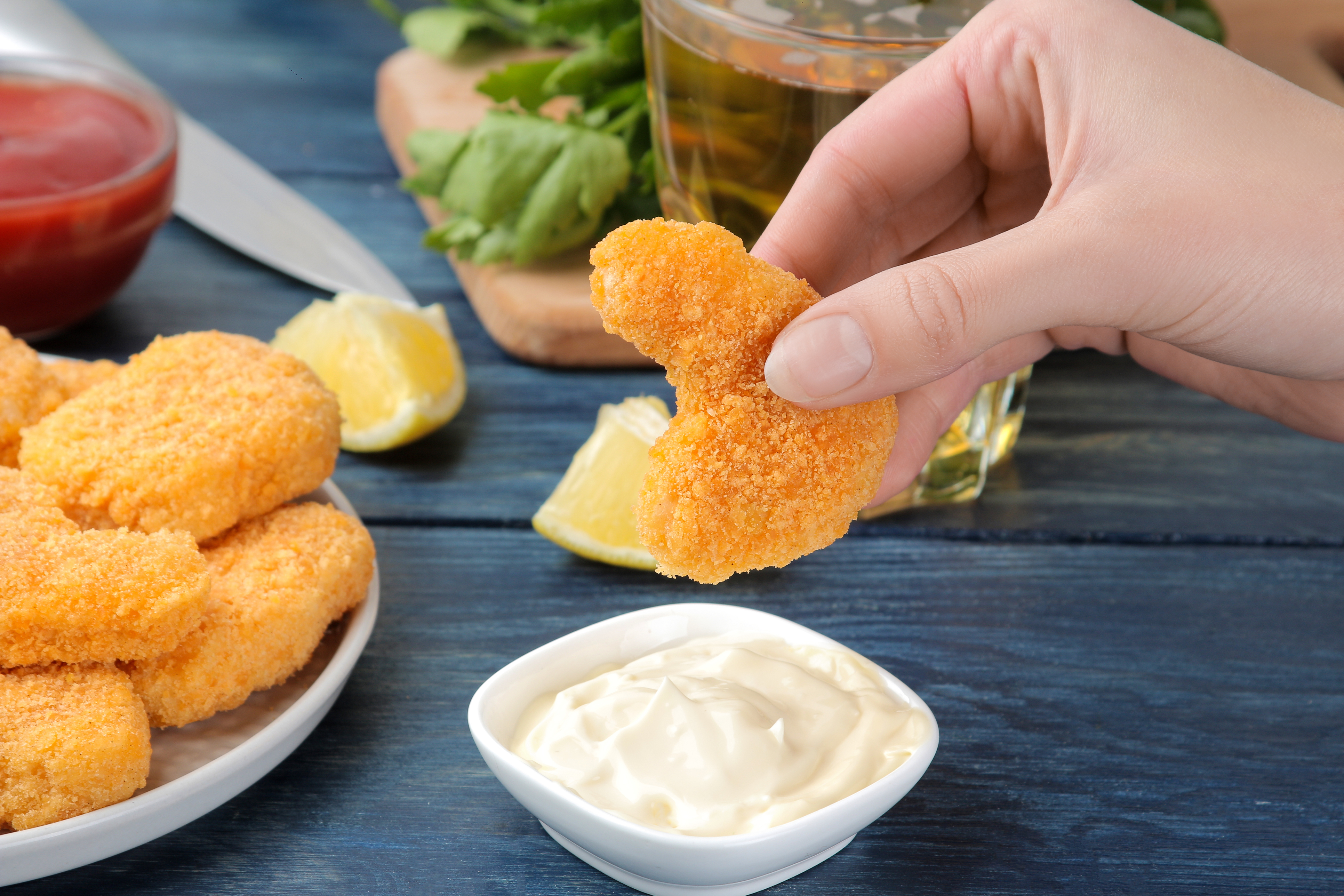 Girl dunks chicken nuggets in white sauce close-up on blue wooden background. fast food